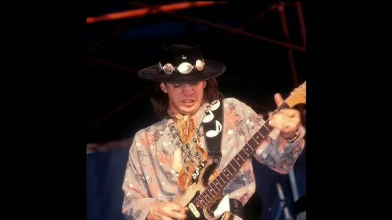 Iconic blues guitarist Stevie Ray Vaughan wears his signature black hat and plays the guitar on stage.