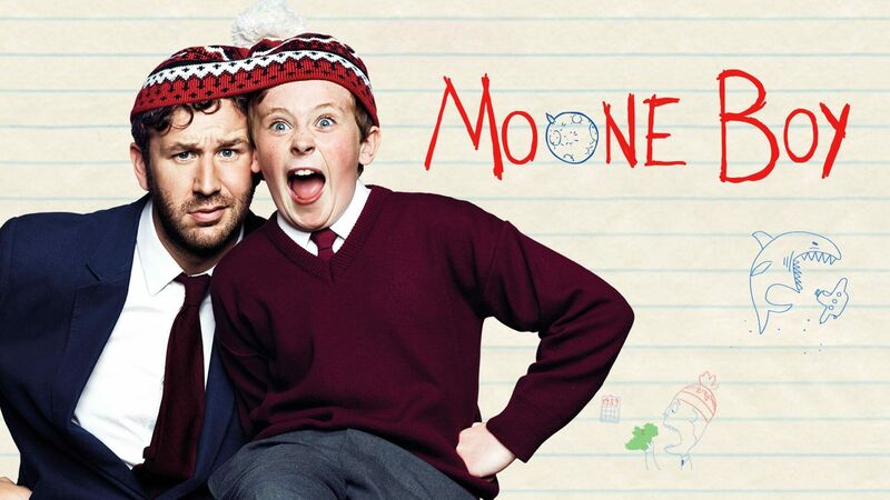 Image shows a man looking worried and a young boy making a goofy face. They have both of their heads fitted into a winter knit hat. The title of the program is Moone Boy.